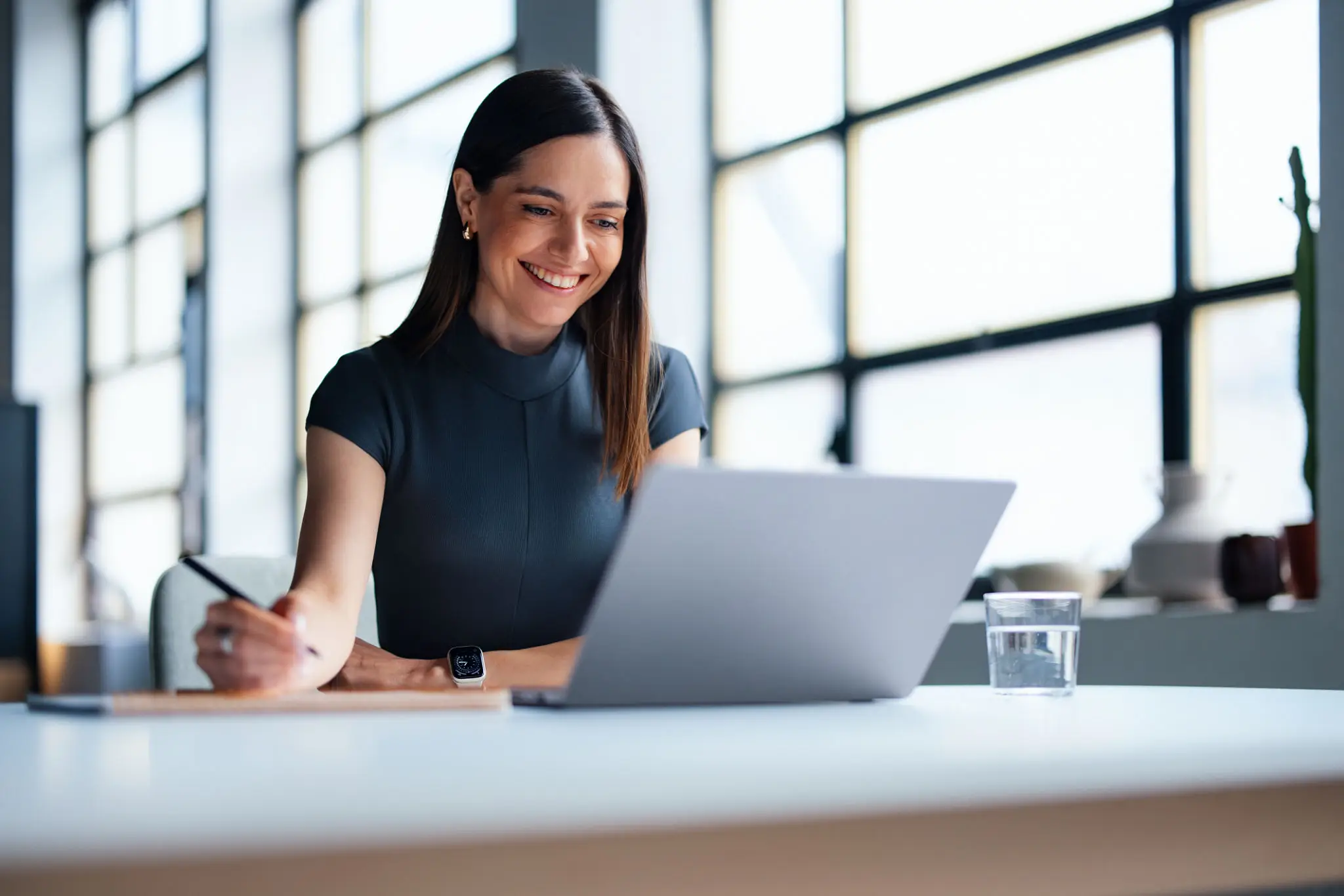Woman working on a laptop with a smile in a bright office.